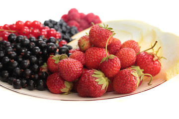 A plate of fruits: strawberries on the forefround and melon, black currants, red currants, bilberries, raspberries on the background
