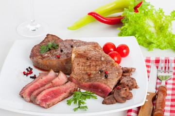 Portions of grilled juice fillet steak served with tomatoes and mushroom sauce on white plate