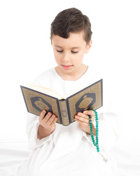 Muslim young boy reading Quran and holding rosary - high key
