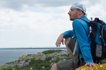 Man sitting on the rock against the background of the sea and somber sky