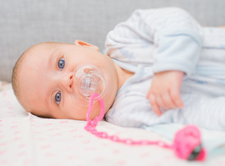 Newborn little baby with dummy on the bed.