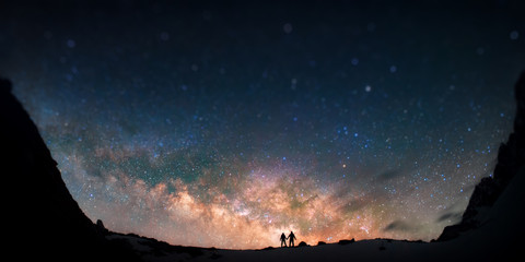Universe for two. Two people are standing together holding hands against the Milky Way in the mountains.  - obrazy, fototapety, plakaty