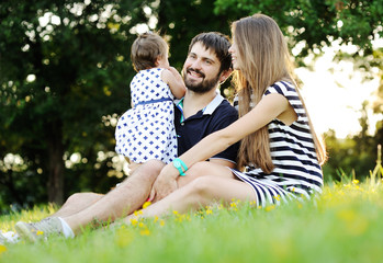 Fototapeta premium Young family relaxing in the park on the grass. little girl sitt