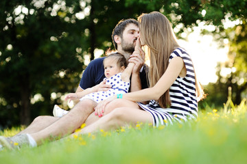 Young family relaxing in the park on the grass. Mom and dad kiss
