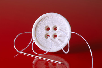 Button, a needle and a thread on red