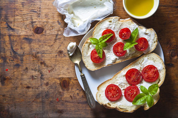 Bruschetta with soft cheese, basil and cherry tomatoes on a wood