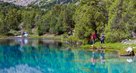 Pristine mountain lake Group of hikers walks along the shore of mountain lake with vivid blue green turquoise colors and reflection of forest pine-trees and mountain valley