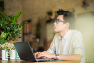 Young asian man drinking coffee in cafe and using laptop compute