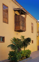 Photography of a house with windows balcony and green plants in front on a sunny day