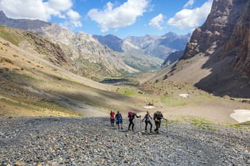 Group of hikers on trail Mountain landscape and people walking with poles backpacks and other gear along dusty Asian trail with green grass and orange rocks around