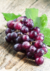 Round purple grapes with leaves on the old wooden table, selecti