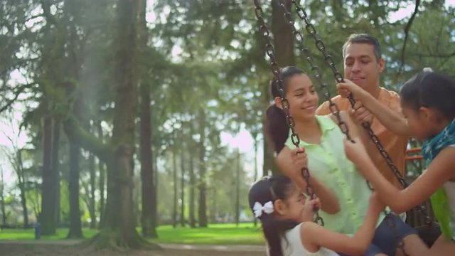 Father pushing his daughters on a tire swing in a park
