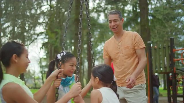 Father pushing his daughters on a tire swing in a park
