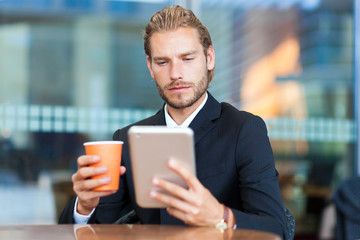 Handsome businessman enjoying a cup of coffee and looking his tablet