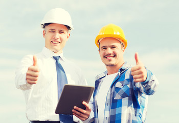smiling builders in hardhats with tablet pc