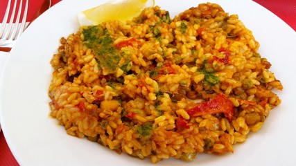 Spanish vegetable paella dish with red pepper and tomato on white plate