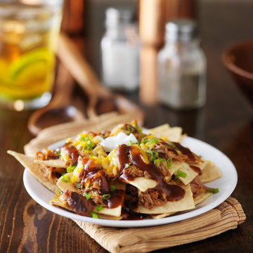 barbecue pulled pork nachos with sourcream, green onions and melted cheese