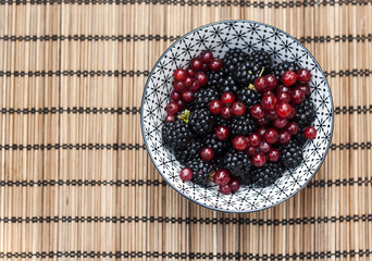 bowl with wild blackberries and redcurrants on a bamboo tableclo