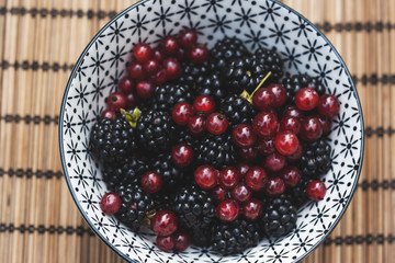 bowl with wild blackberries and redcurrants on a bamboo tableclo