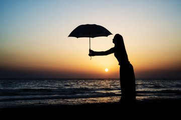 Young girl with an umbrella on the beach at the sunset time