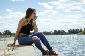 Fototapeta na wymiar Chica adolescente posando en el embarcadero. Adolescente rubia de quince años como modelo. Chica rubia de pelo largo al lado del rio en verano. 