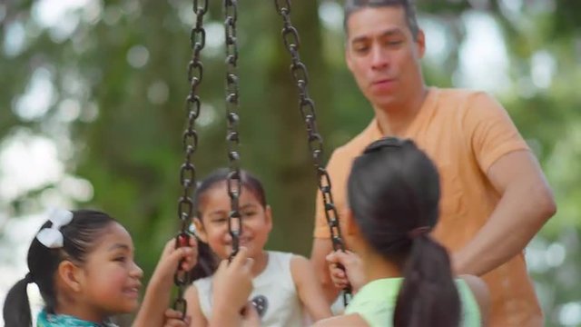 Father pushing his daughters on a tire swing in a park
