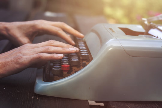 male hands writing with an old blue typewriter, vintage stock photo
