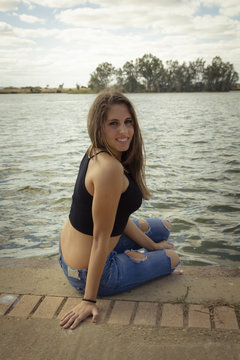 Chica adolescente posando en el embarcadero. Adolescente rubia de quince años como modelo. Chica rubia de pelo largo al lado del rio en verano. 