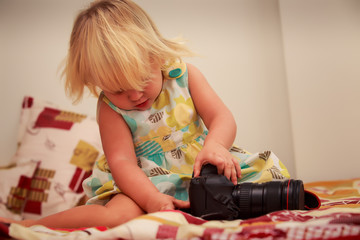 little blonde girl examines camera against white wall