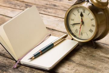 Open small notebook with fountain pen and old-fashioned alarm clock behind