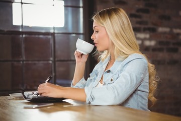 Pretty blonde drinking coffee and writing in planner