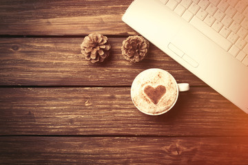 Cup of coffee with heart shape and laptop computer