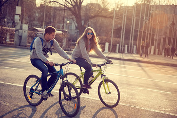 Plakat young couple on bicycles in the city at sunset