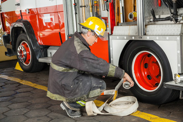 Fototapeta premium Firefighter Crouching While Holding Hose By Truck