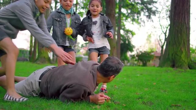 Young girls piling on their father in a park