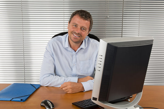 Close-up portrait of a balack and grey haired man with computer at desk