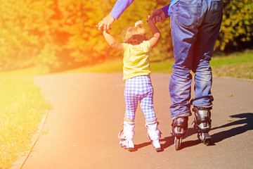 father teaching little daugther to roller skate in summer