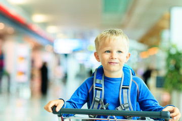 Fototapeta na wymiar Happy cute little boy at airport riding on luggage cart