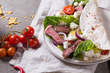 Mexican tortillas with green fresh salad filling, beef, onions, tomatoes with gucamole and tortilla chips on te vintage board