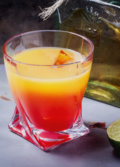 Tequila Sunrise served in a highball glass with ice, grenadine and lime