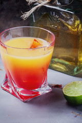 Tequila Sunrise served in a highball glass with ice, grenadine and lime
