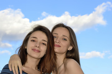 Two beautiful young women standing over blue sky and hugging