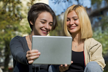 Two beautiful young women browsing tablet outside.