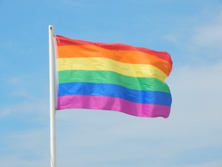 Regenbogenfahne der Schwulenbewegung vor blauem Himmel, flatternd im Wind
