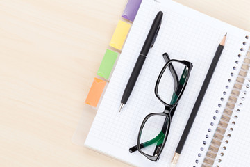 Office table with glasses over notepad, pen and pencil