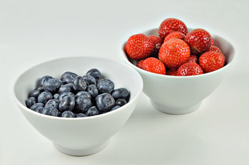 Blueberries and Strawberries in a Bowl / close up of two white bowls with strawberries and blueberries on a white background 