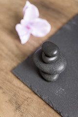 Pile of four spa stones with a fresh orchid flower next to it on a slate tray