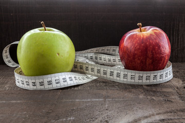  apple surrounded by a measuring tape referring to diet and health concept on wooden background