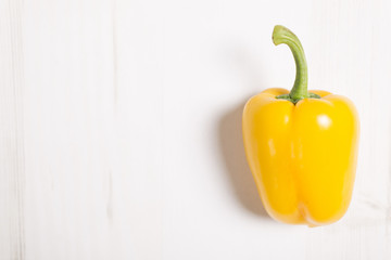 Fresh yellow bell pepper on a light wooden kitchen surface
