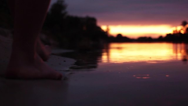 girl comes into the water at sunset. close up of girl's feets